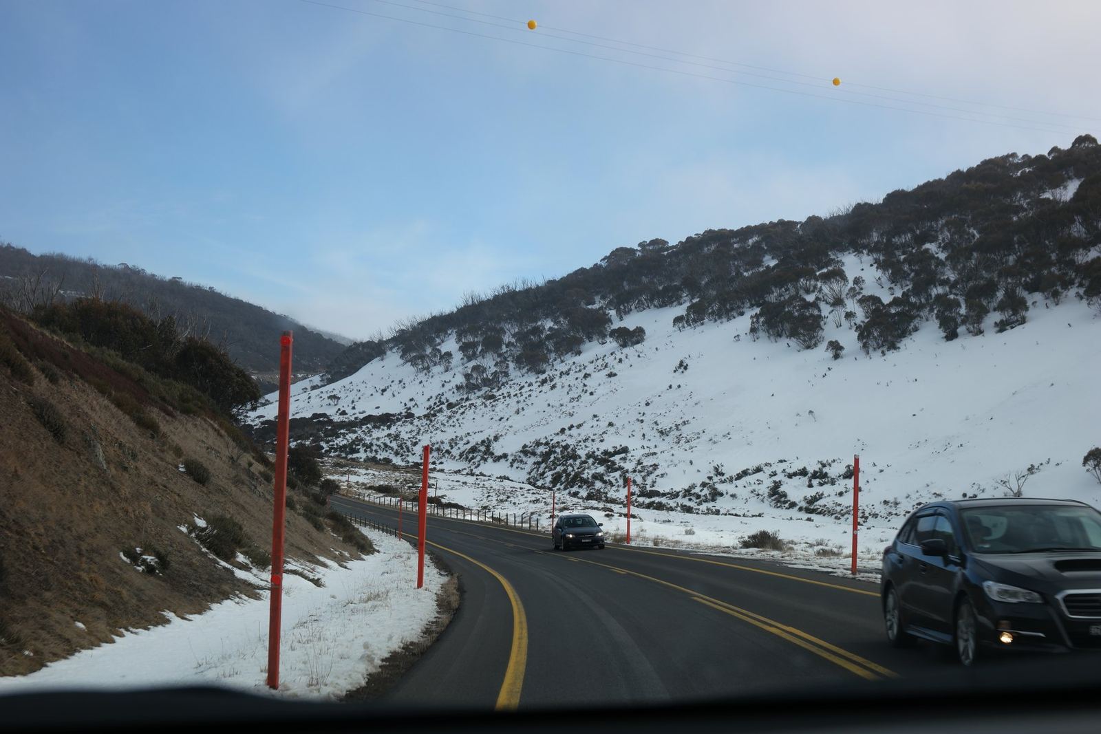Snow poles lining a cleared road climbing into the mountains, snow on both verges