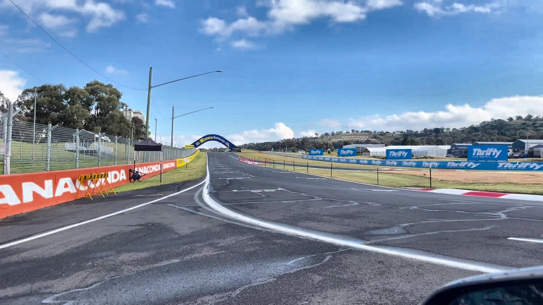 The empty pit straight at Mount Panorama seen from a car at the entrance, sponsor hoardings along both sides and an arch over the track ahead