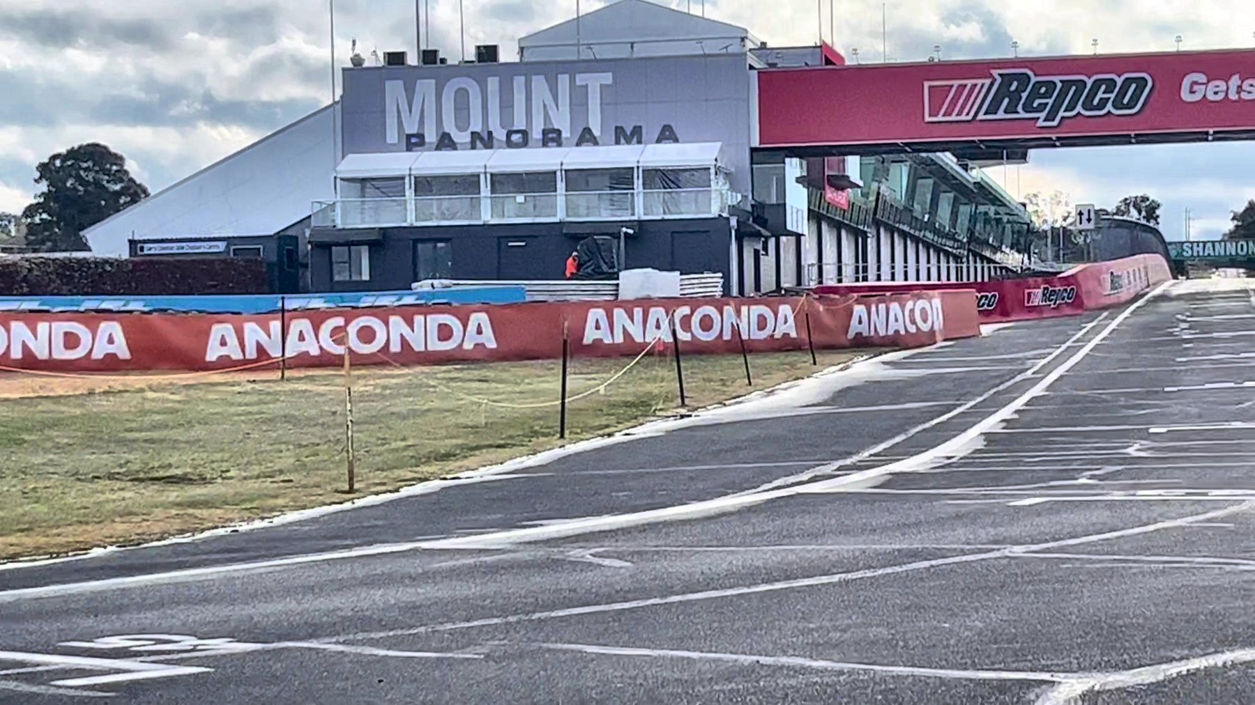 The Mount Panorama pit building and control tower beside the track, with a sponsor bridge spanning the circuit beyond it