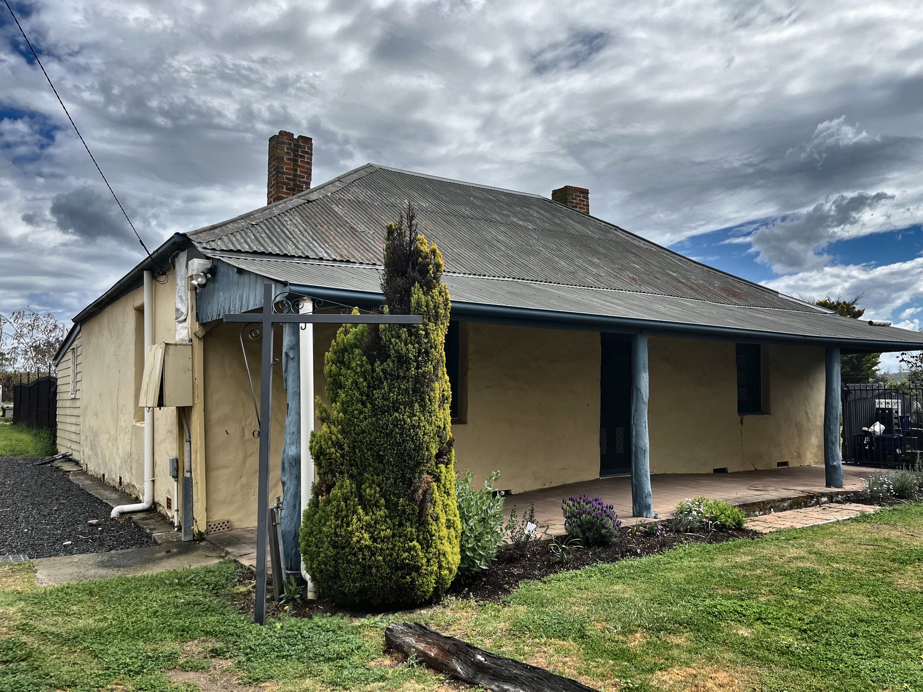 A low rendered earth cottage with a corrugated iron roof and a timber-posted verandah