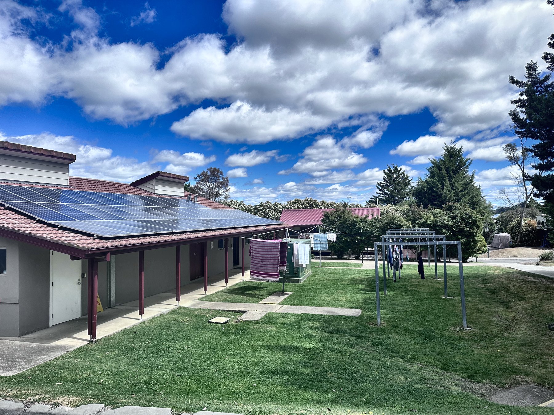 A single-storey amenities block with solar panels across its roof, lawn and washing lines in front
