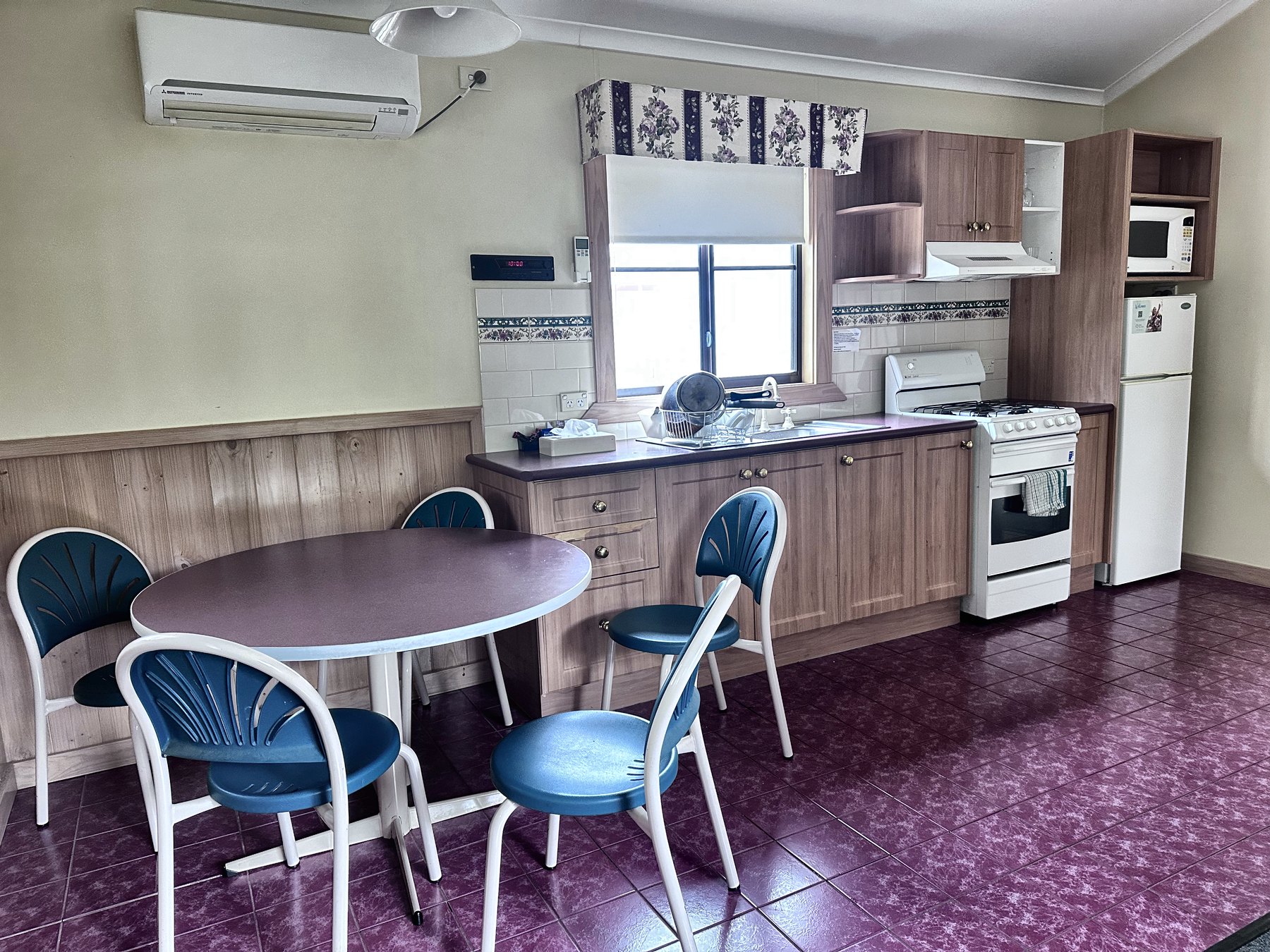 A cabin kitchen with a full freestanding oven and cooktop, overhead cupboards, microwave and a round dining table with four chairs
