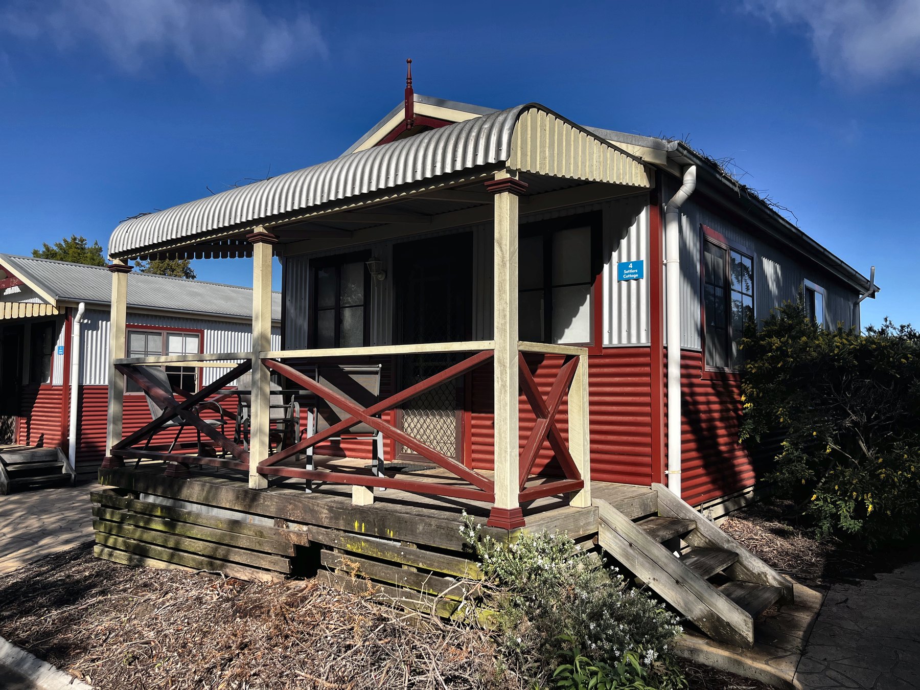 A red and cream weatherboard cabin with a pitched corrugated verandah roof and timber steps