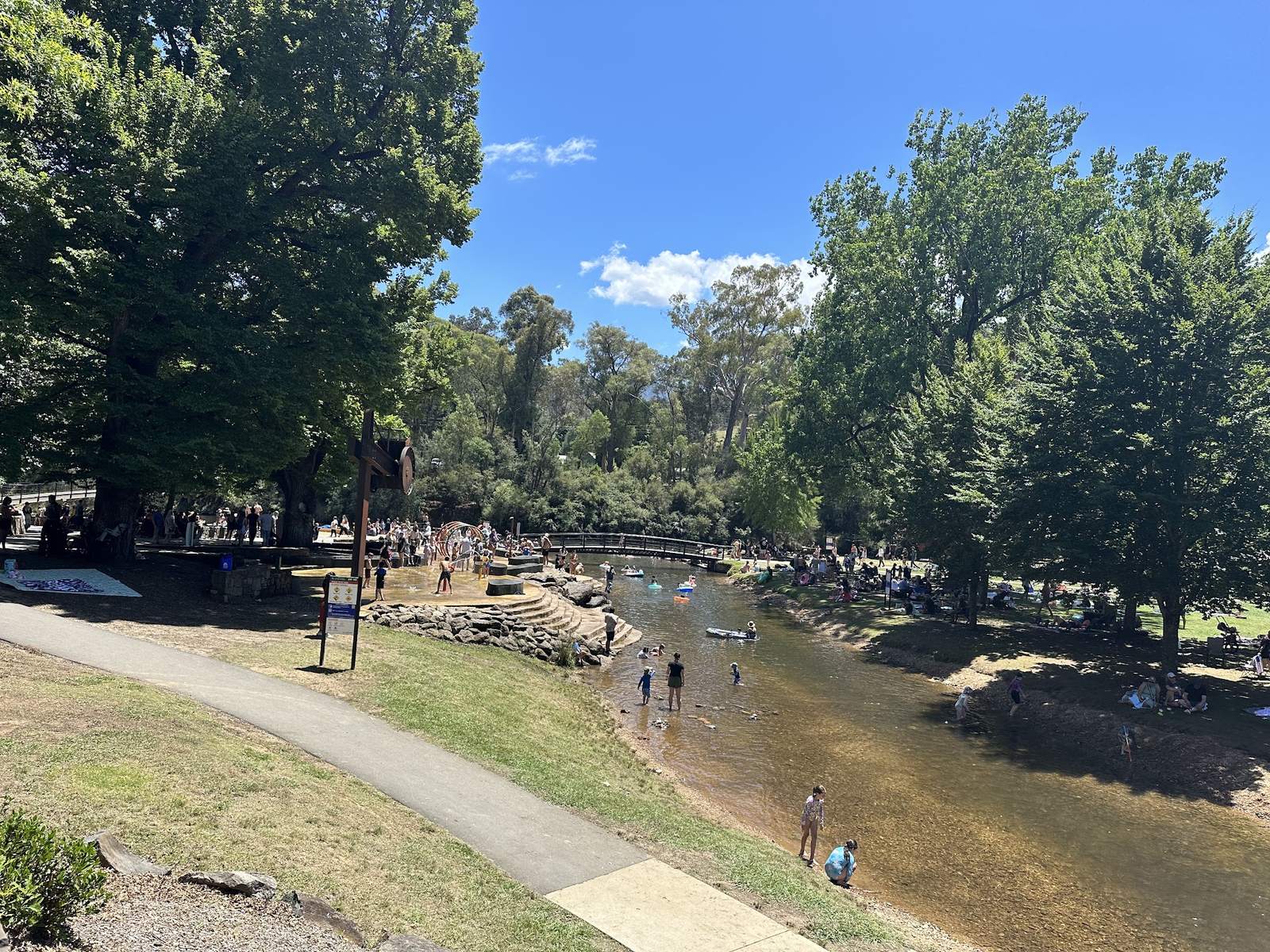 A wide view down over the splash park, the stepped stone edge and the river beyond, with the footbridge and the town behind