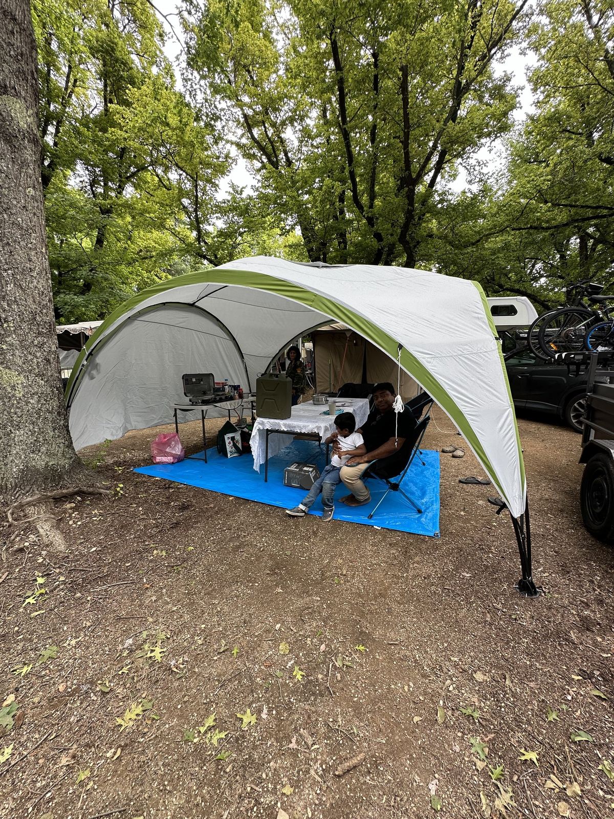 A white shade shelter pitched over the camp kitchen on bare ground, gear laid out on a blue mat underneath