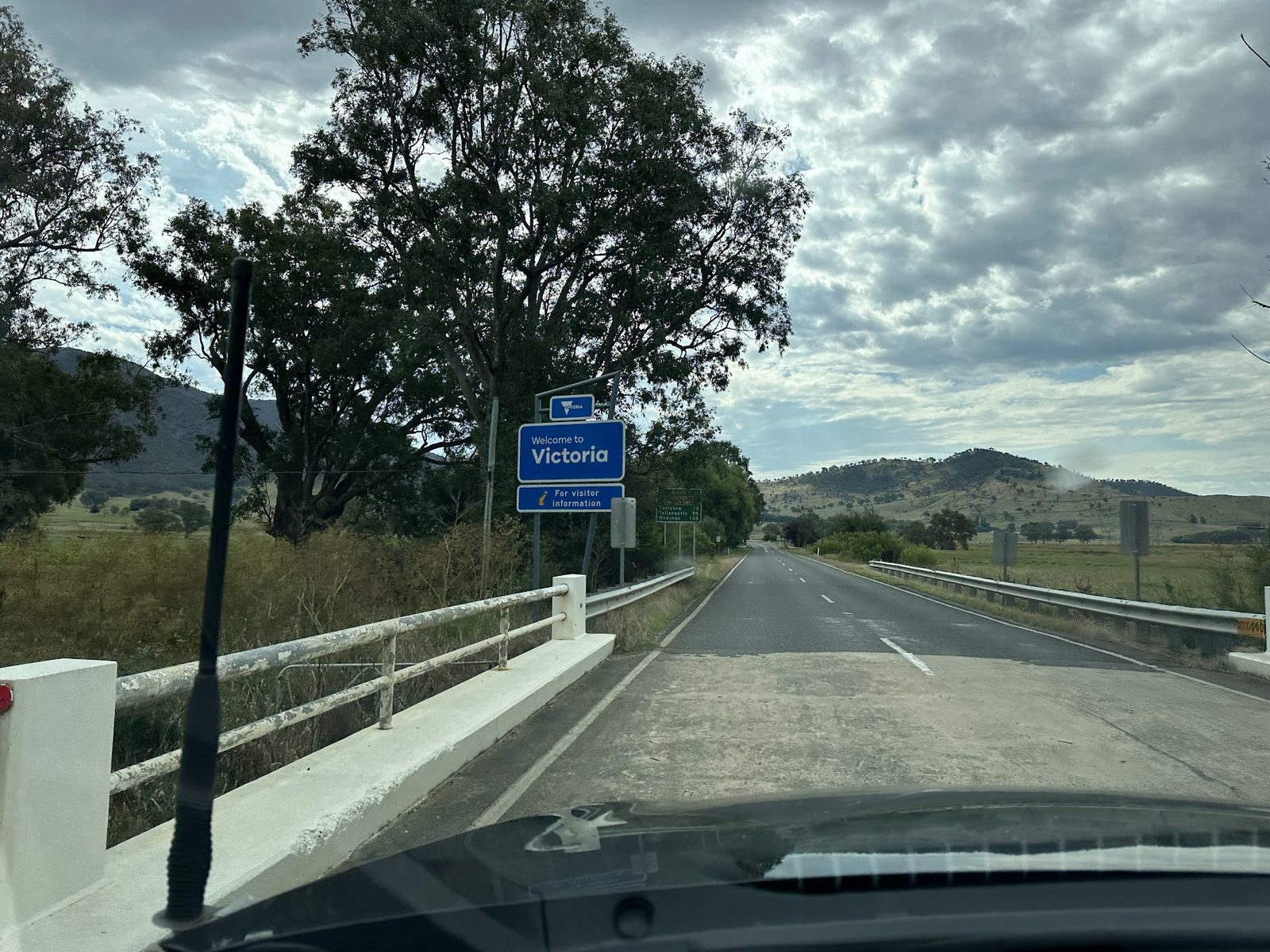 A roadside Welcome to Victoria sign photographed from a moving car, with distances to Corryong, Tallangatta and Wodonga below it