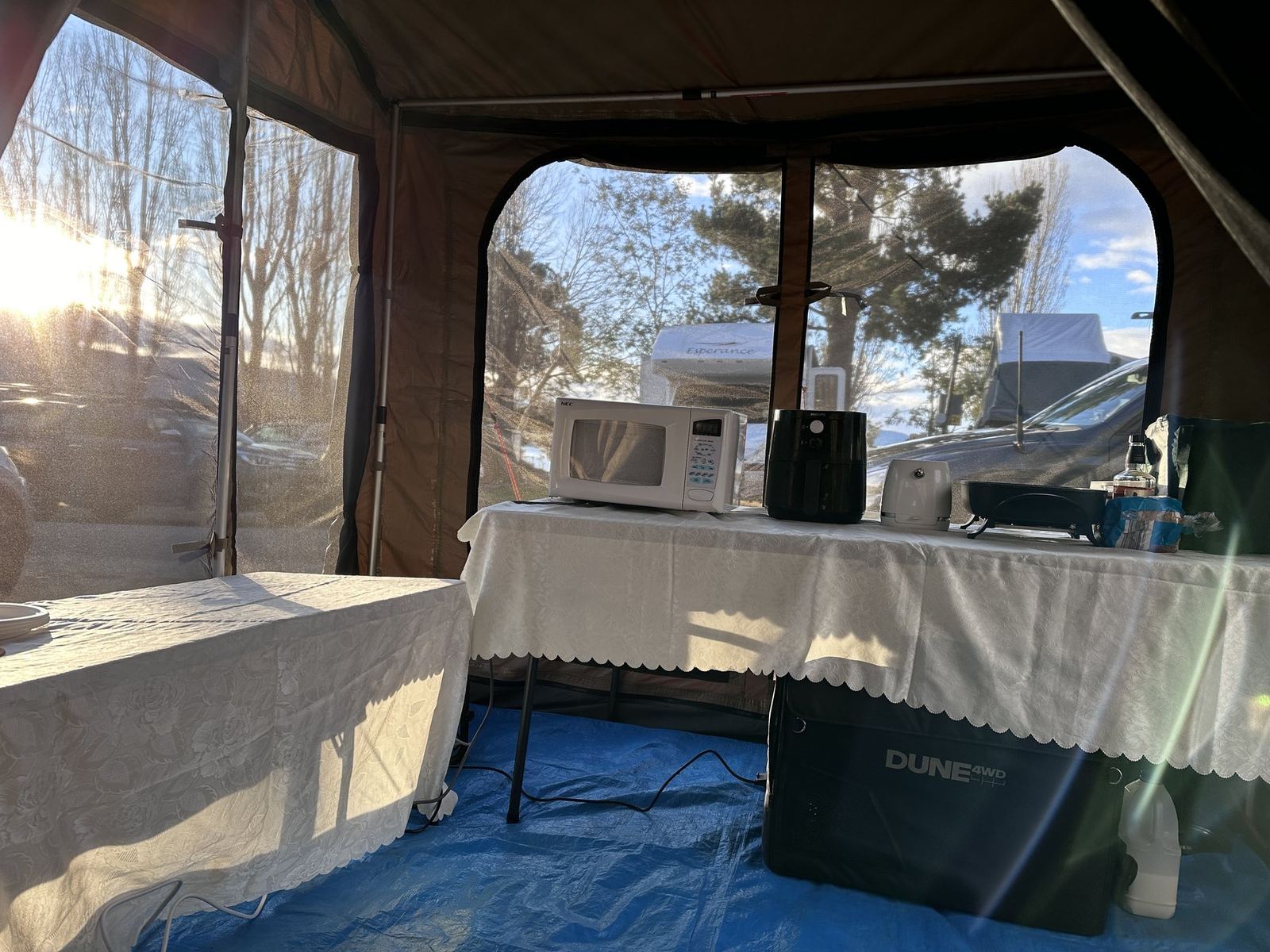 Low winter sun through the mesh window of a canvas tent, falling across the camp kitchen table