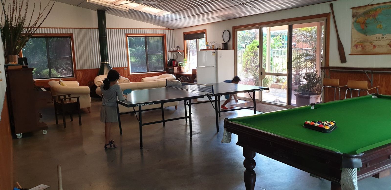 A large communal room with a pool table, table tennis table and windows to the bush on two sides
