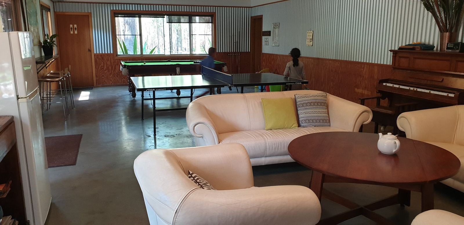 A lounge area with armchairs around a low table, a piano against the far wall and long dining tables beyond