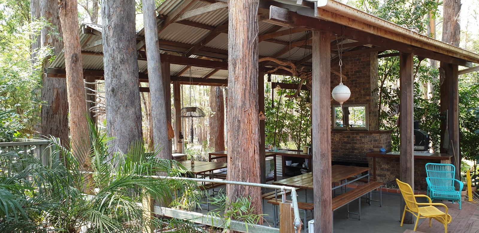 A covered outdoor kitchen and eating area with brick piers, open to the bush on all sides