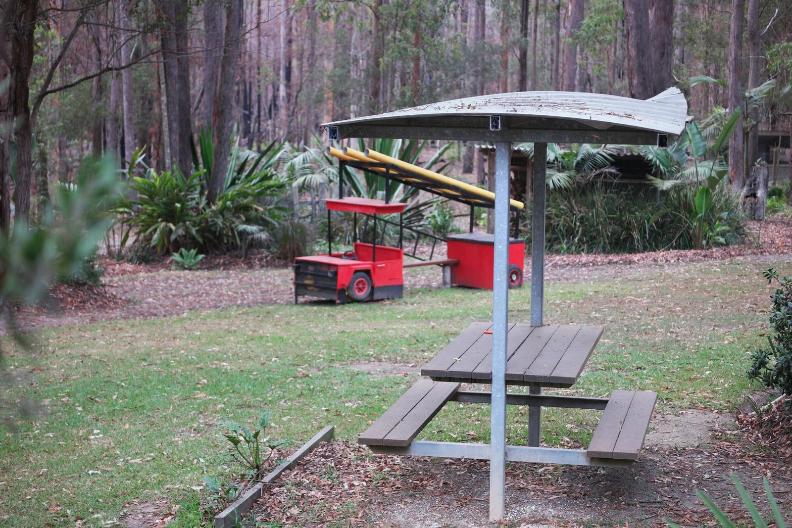 A picnic table under a curved metal shelter among the gum trees, karts parked behind