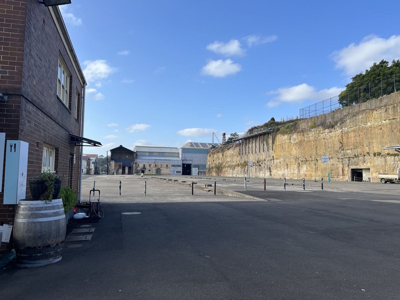 The island's empty industrial yard in the morning, brick buildings, a wine barrel and the cut sandstone cliff behind