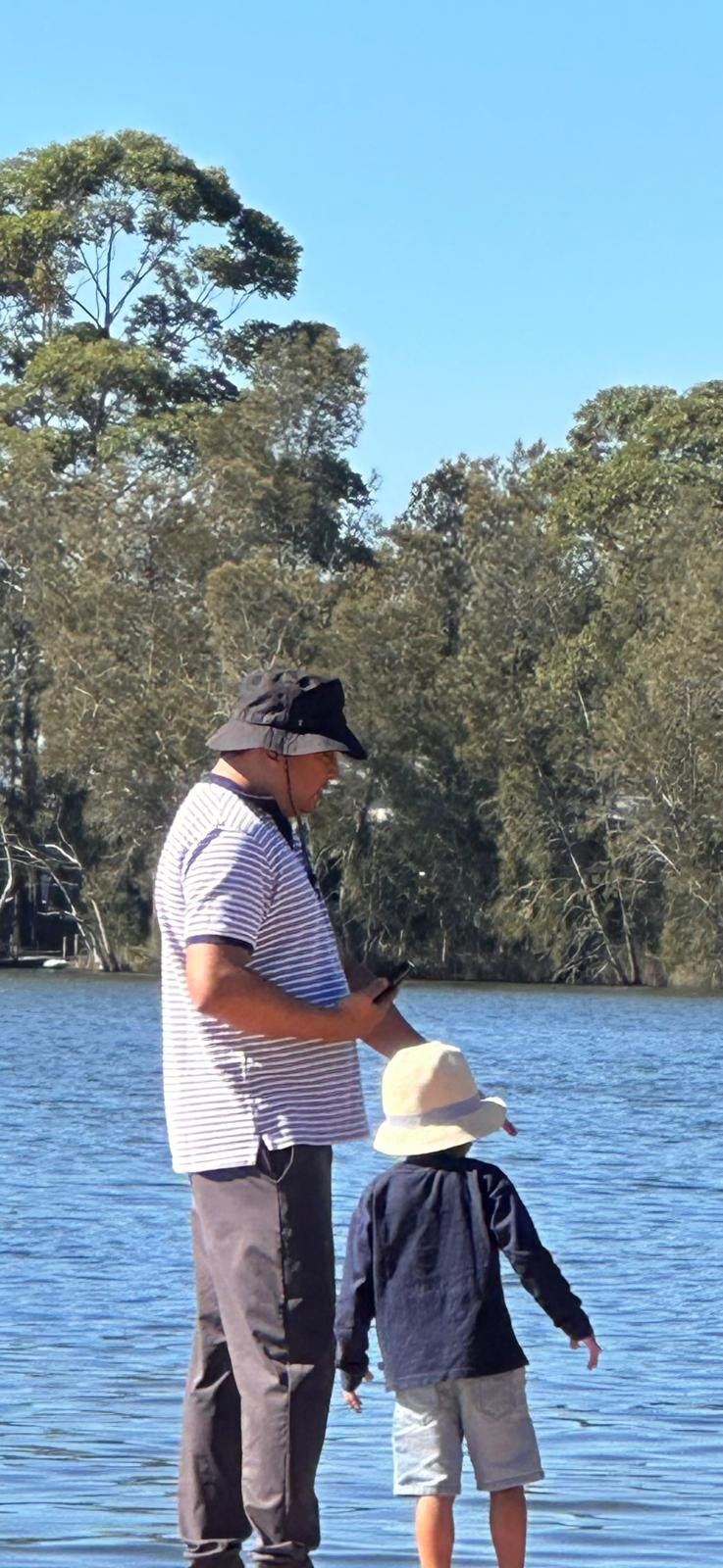 An adult and a small child standing together at the edge of the lake, looking out at the water