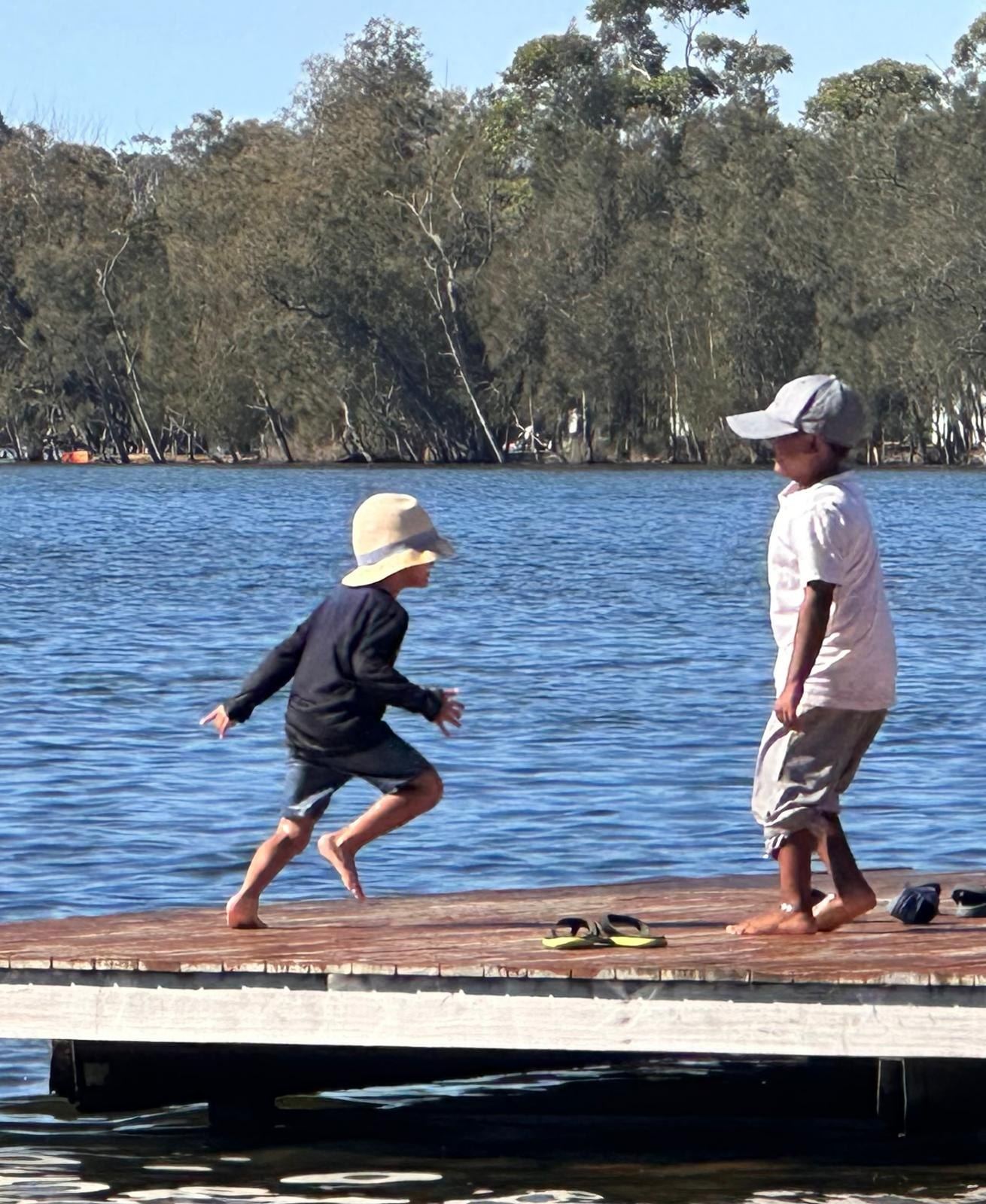 Two children on a timber jetty, one mid-stride about to jump into the lake and the other watching