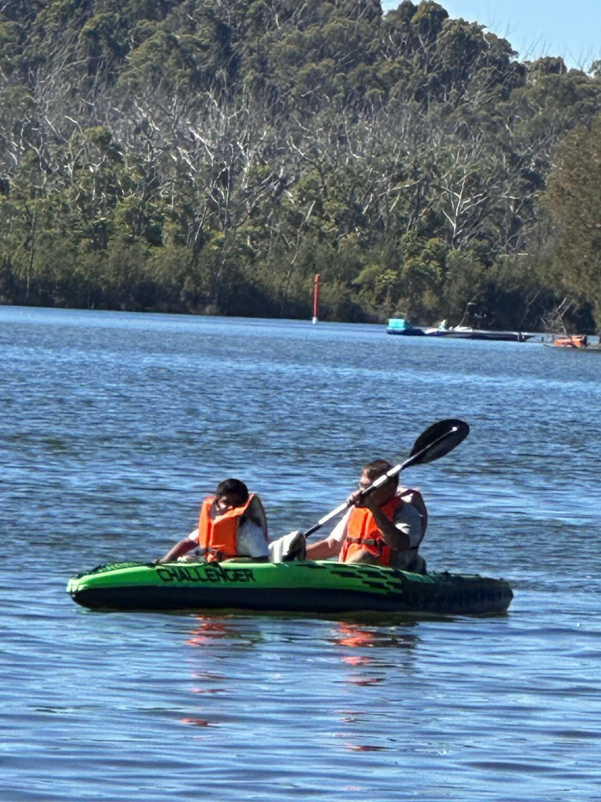 Two children in life jackets paddling the green kayak away from the bank