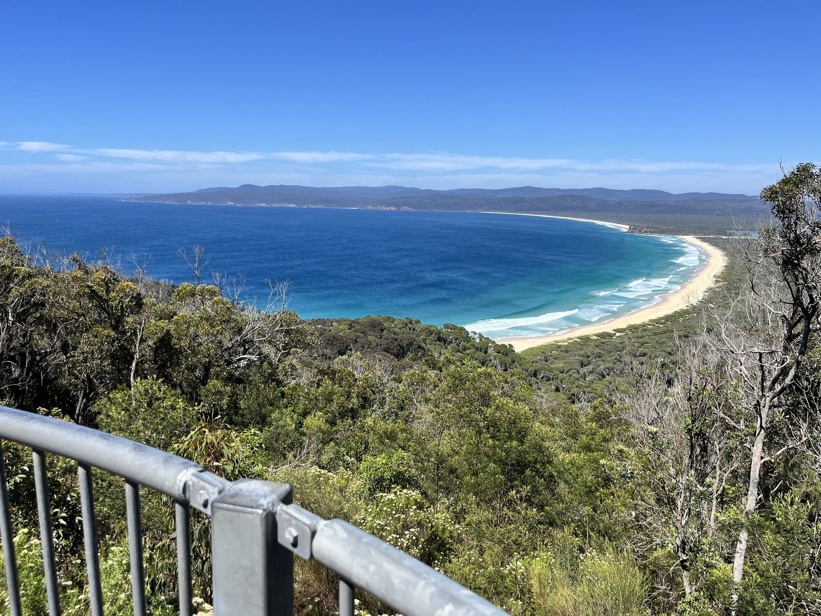 A long white beach curving away below a lookout, deep blue ocean on one side and unbroken forest on the other