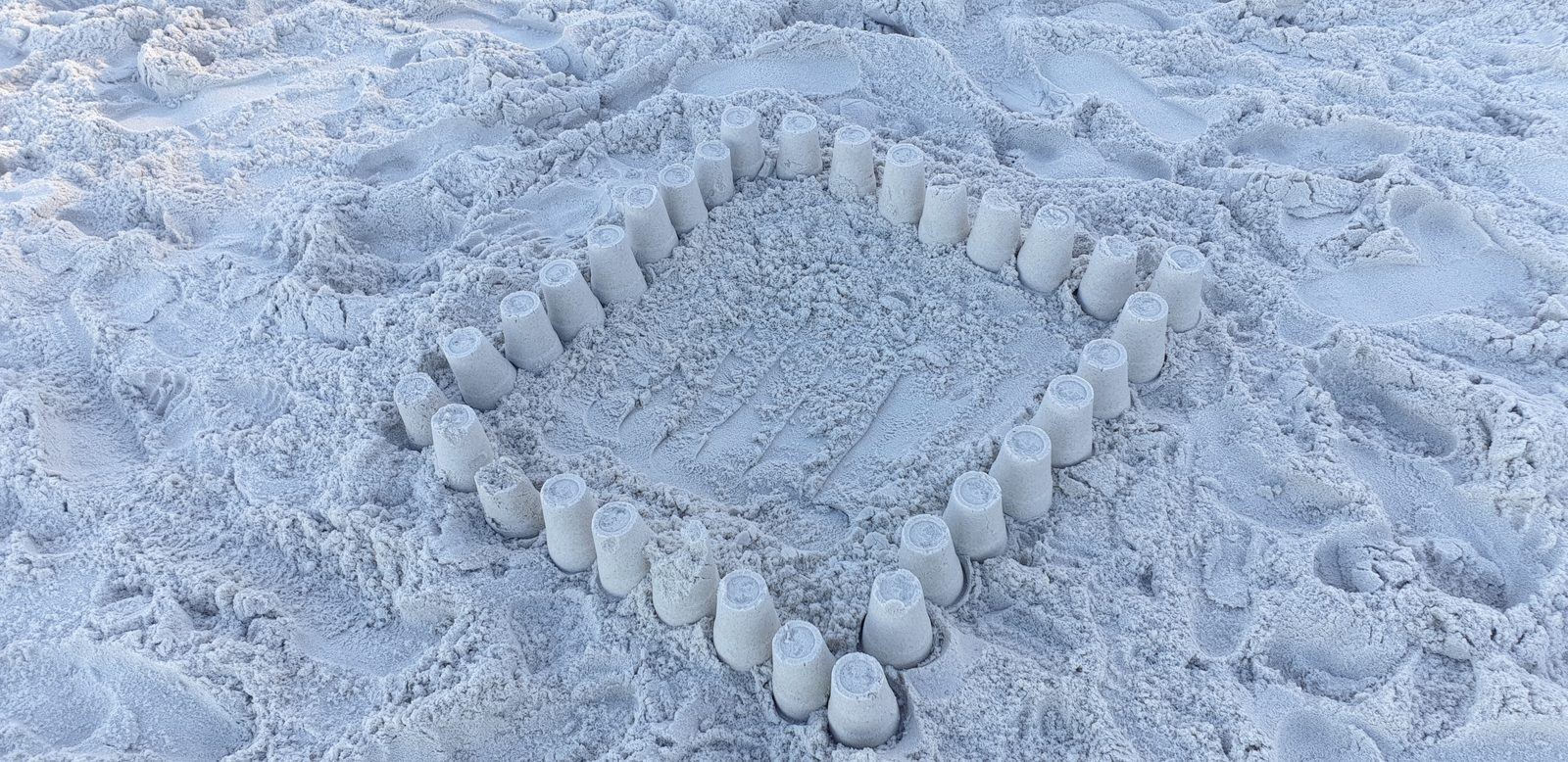 A ring of small sand towers moulded with a bucket, built around a hollow in very fine white sand