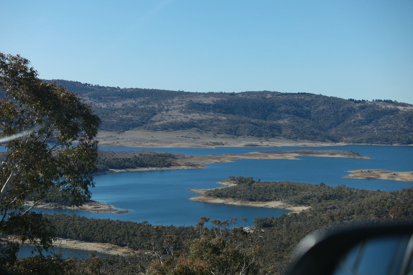 Lake Jindabyne seen from the road, blue water and low scrubby islands under a clear winter sky