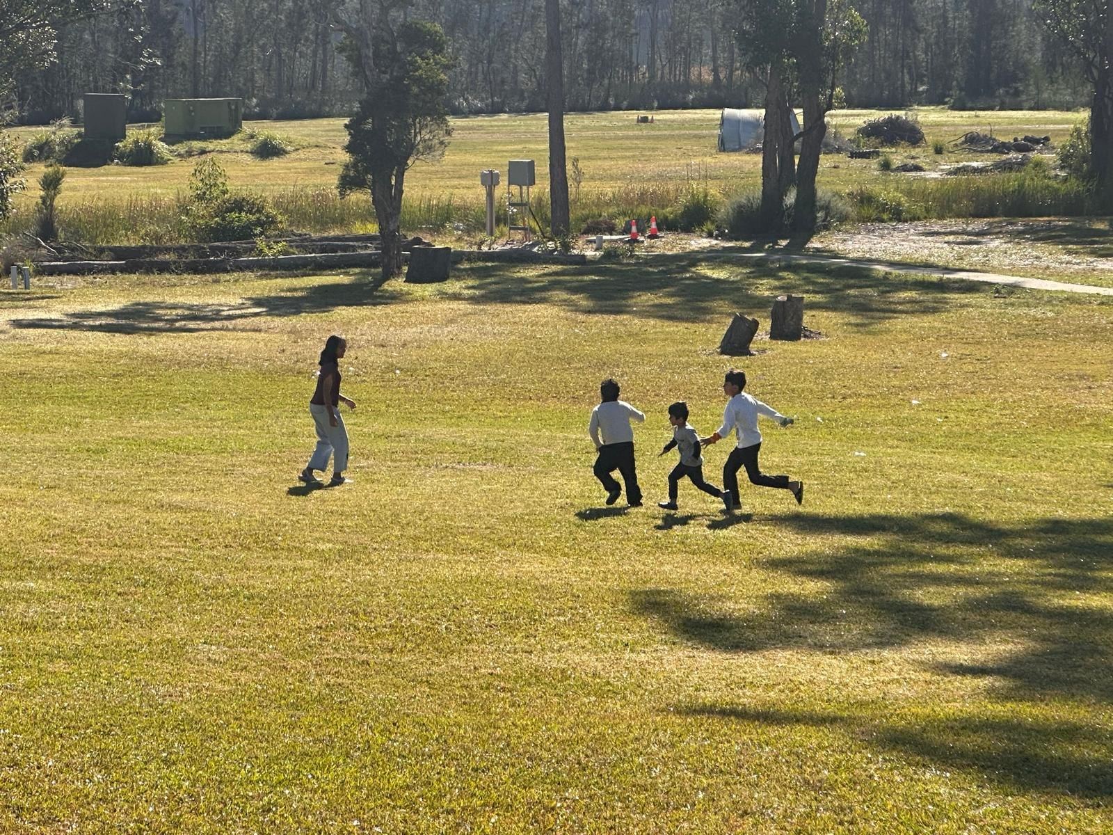 Four people running across the mown grass of the park in late afternoon light, long shadows behind them