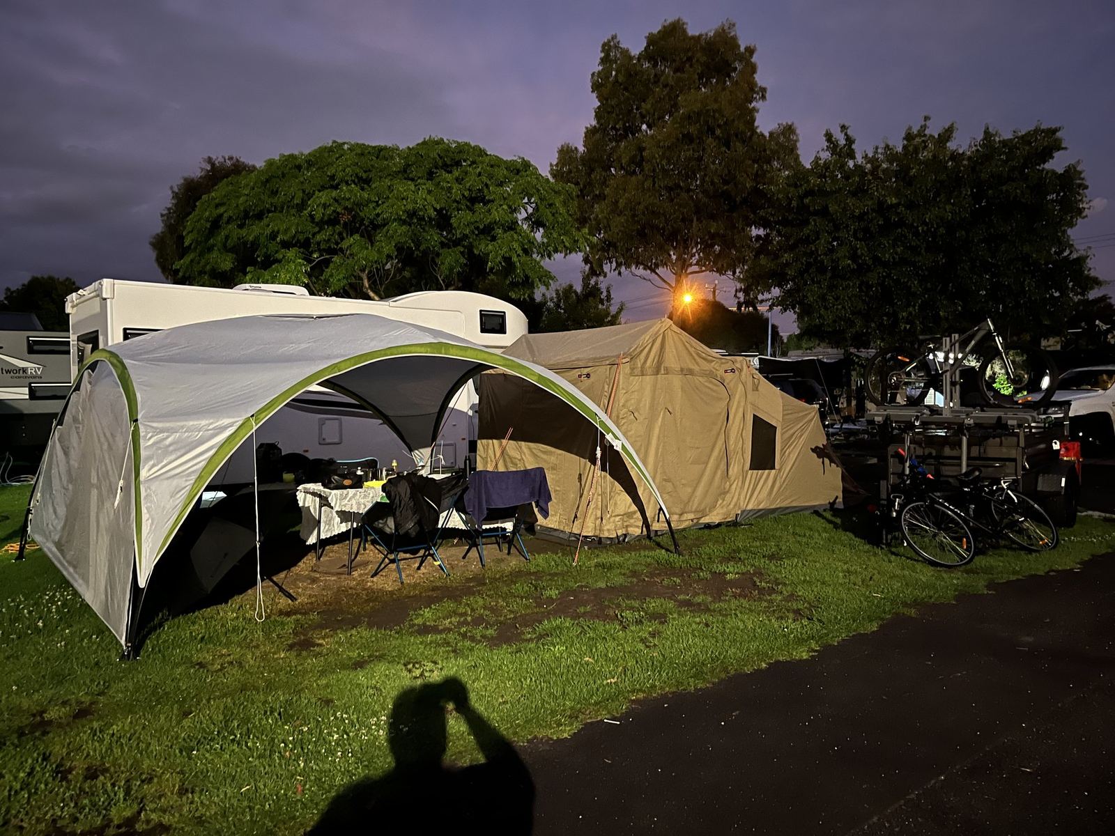 The shade shelter and tent at dusk with the table set underneath and a purple sky above the trees