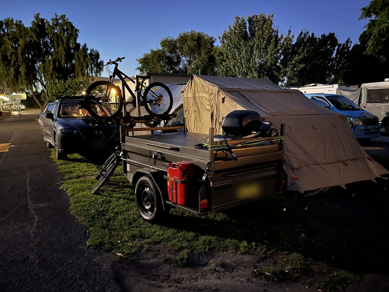 The trailer with a jerry can and roof box, bikes on the rack, in low evening light with vans lined up behind