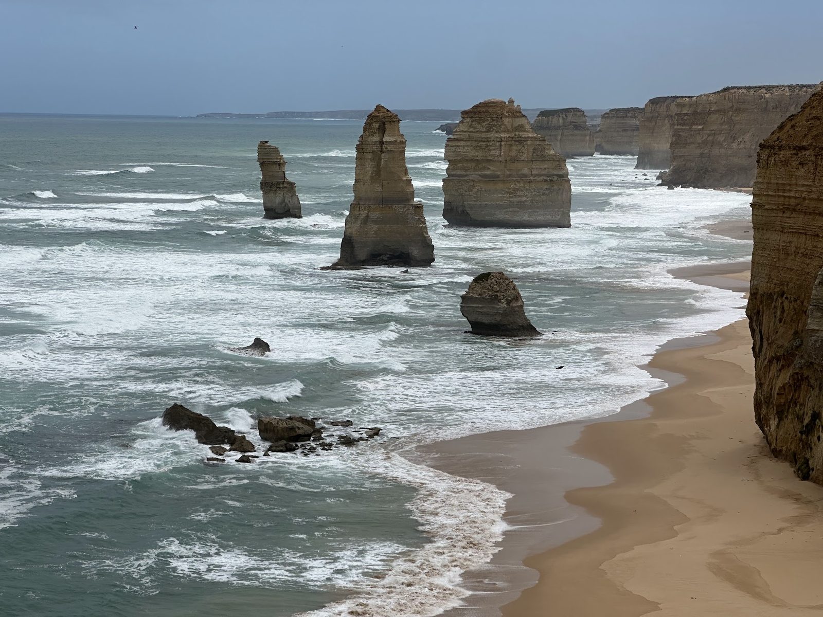 The Twelve Apostles limestone stacks standing off a cliffed coastline under a clear sky, seen from the viewing platform