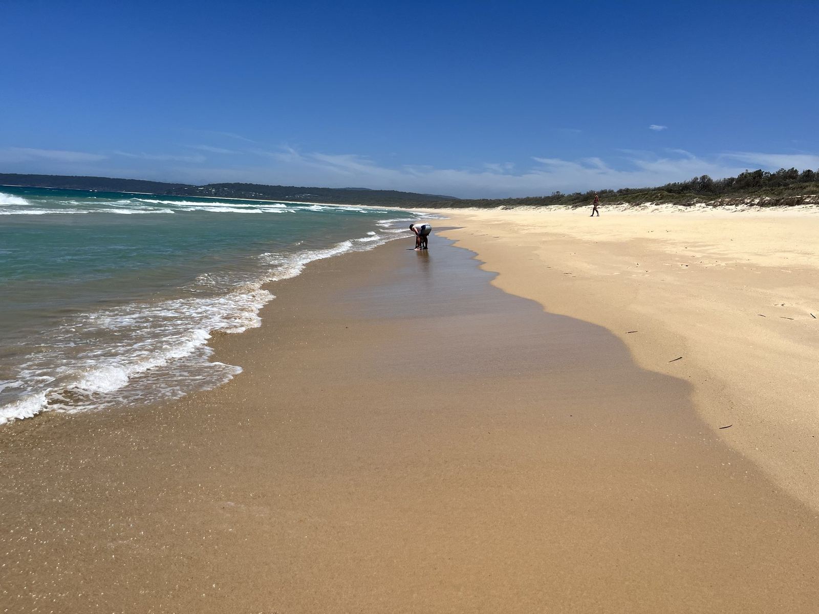 A wide empty beach with wet sand reflecting the sky, one distant figure at the water's edge
