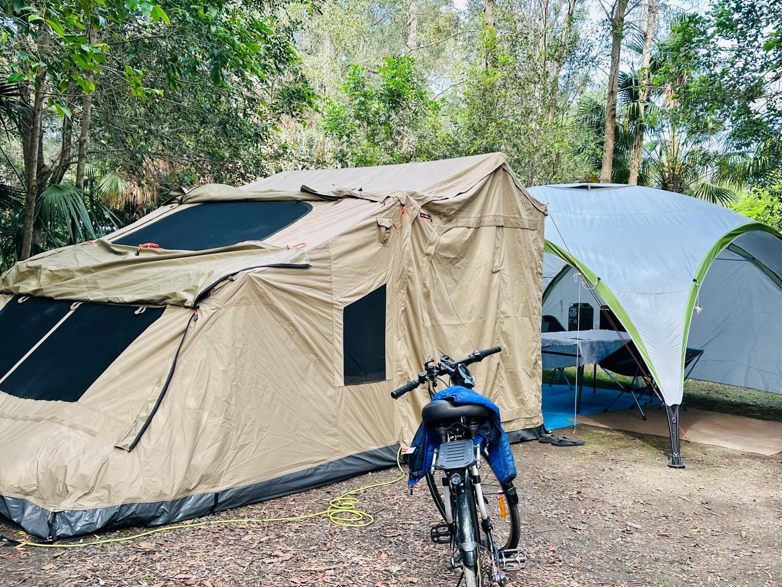 The canvas tent and a shade shelter set up side by side on a shaded site, a bike leaning in front