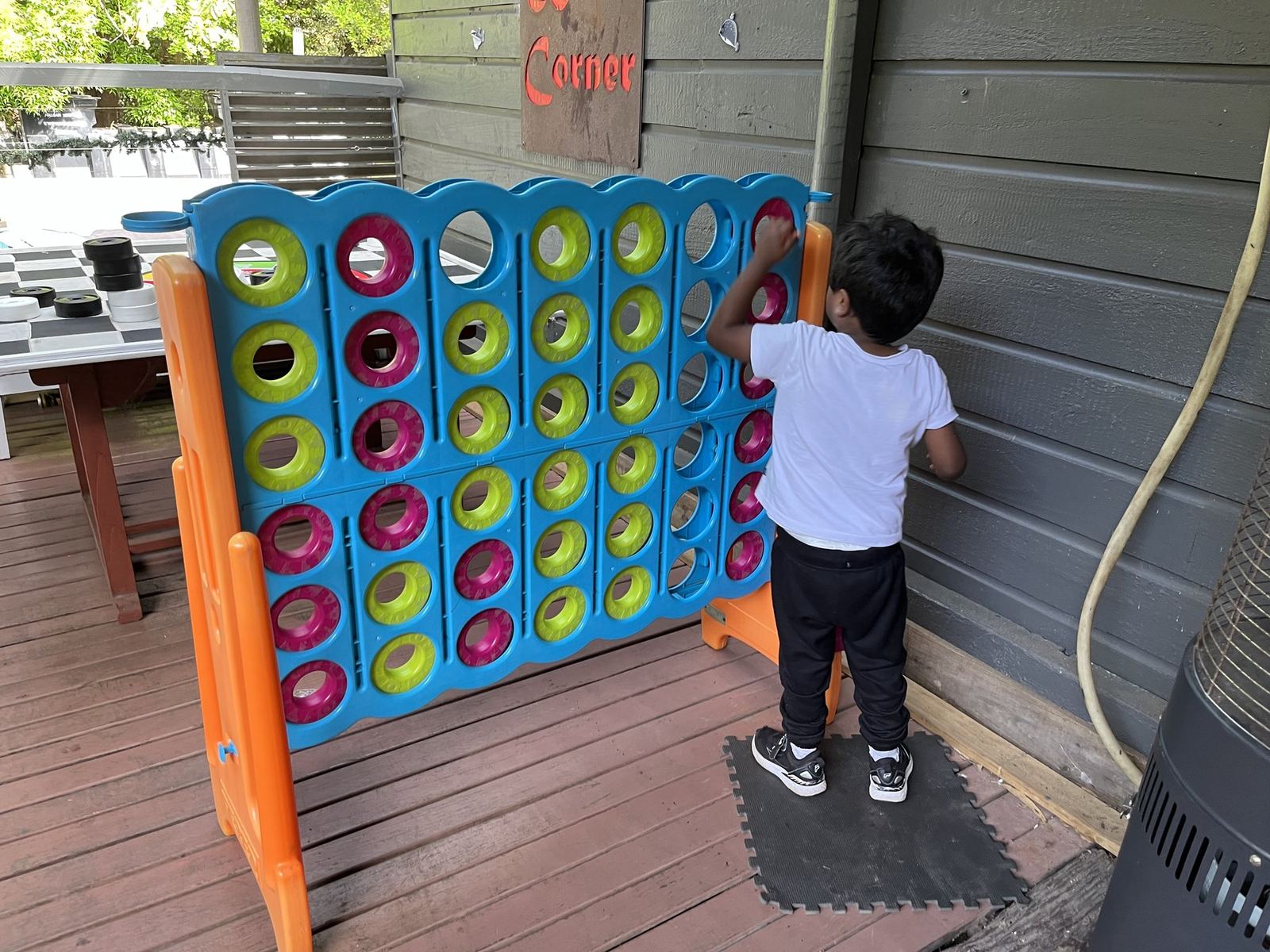 A child playing at a giant wall-mounted Connect Four board on a timber deck in the park's games corner