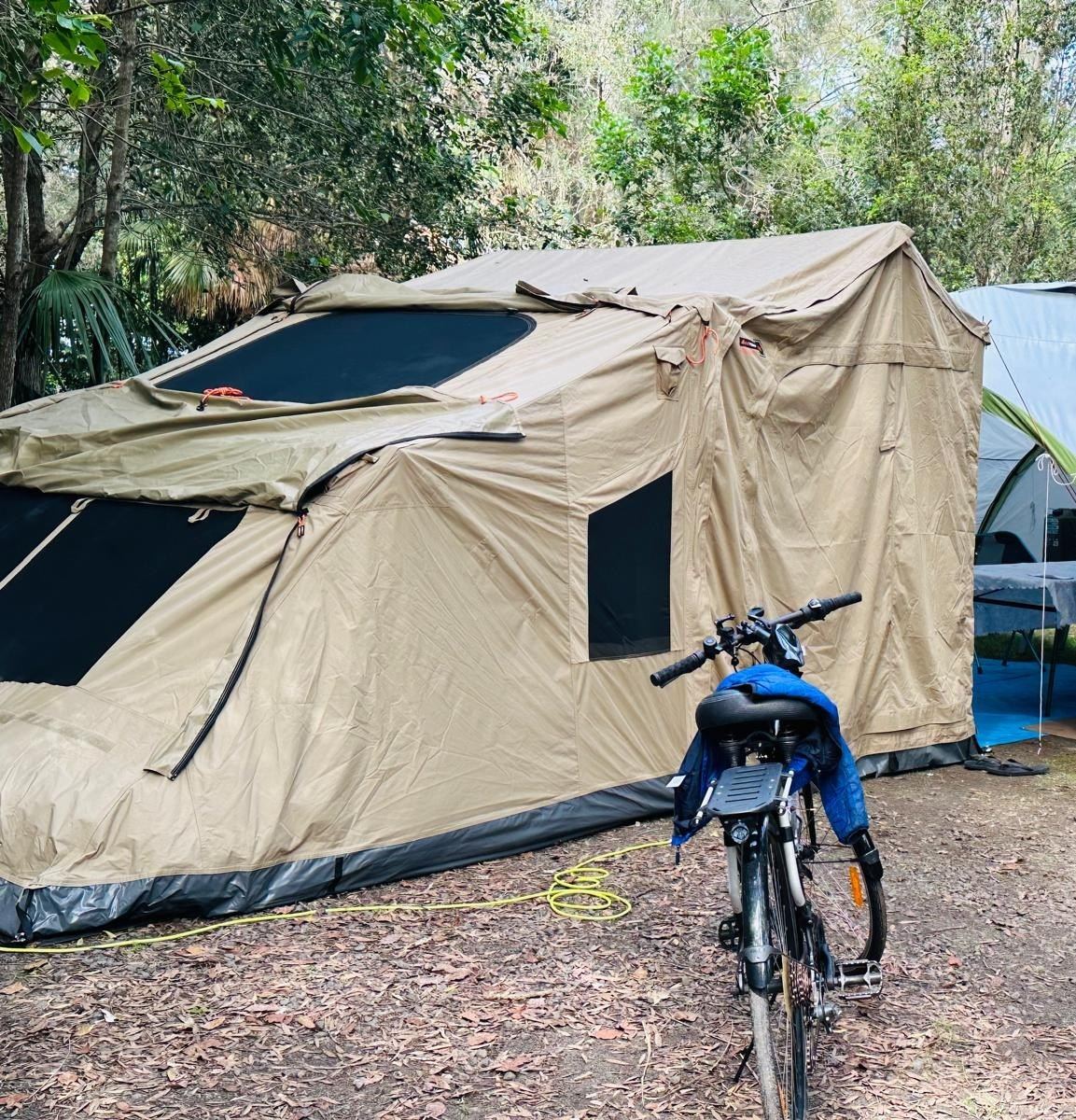 The canvas tent from the front with a bike parked against it and other camps visible through the trees