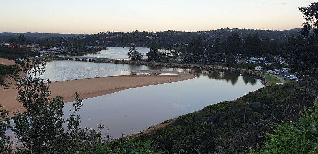 Wide view over Narrabeen Lagoon and its sandbar from high on the headland track, framed by coastal scrub