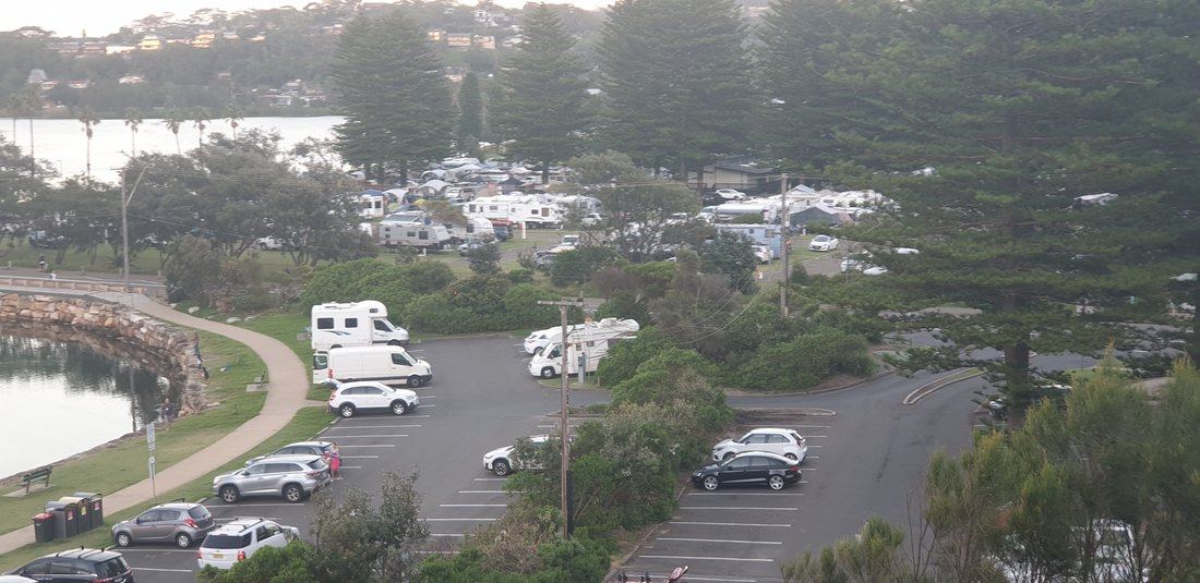 Narrabeen Lagoon and the holiday park seen through morning haze from the headland, campervans parked along the water