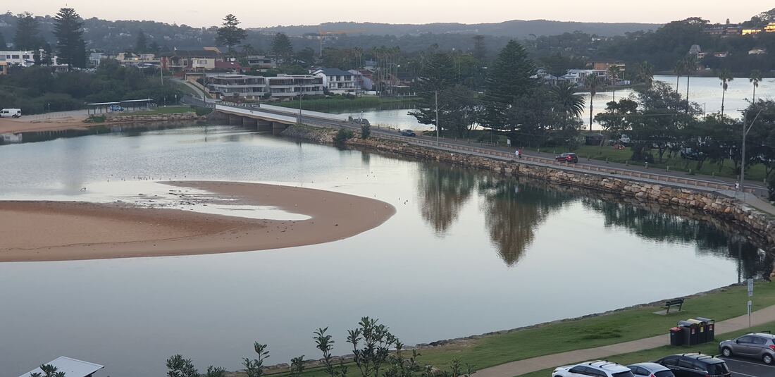 Narrabeen Lagoon at first light, the sandbar curving through still water with the holiday park beyond