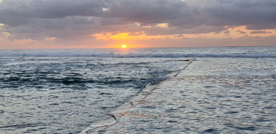 Sun rising over the sea beyond the wall of North Narrabeen ocean pool