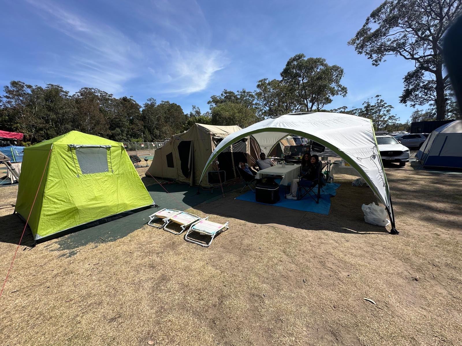 A full camp set-up on dry grass: canvas tent, bright green ensuite tent, white dome shade shelter and camp furniture between them
