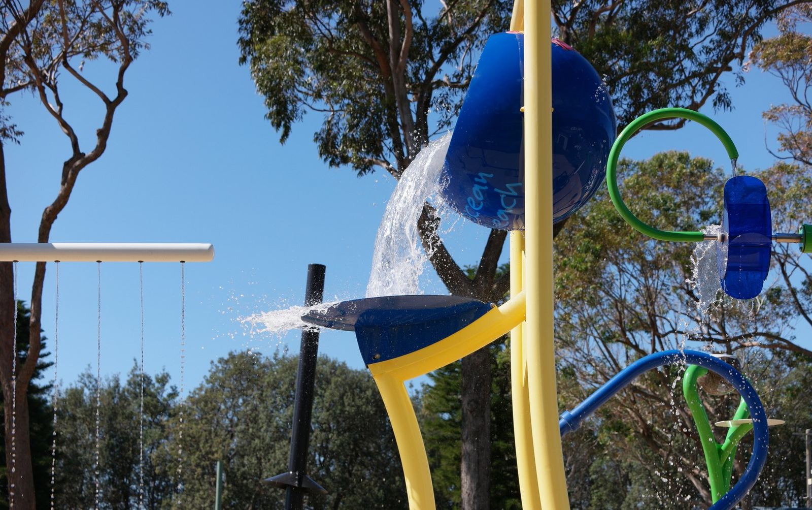 A close view of the splash park's tipping bucket pouring water, blue and yellow structures against the trees