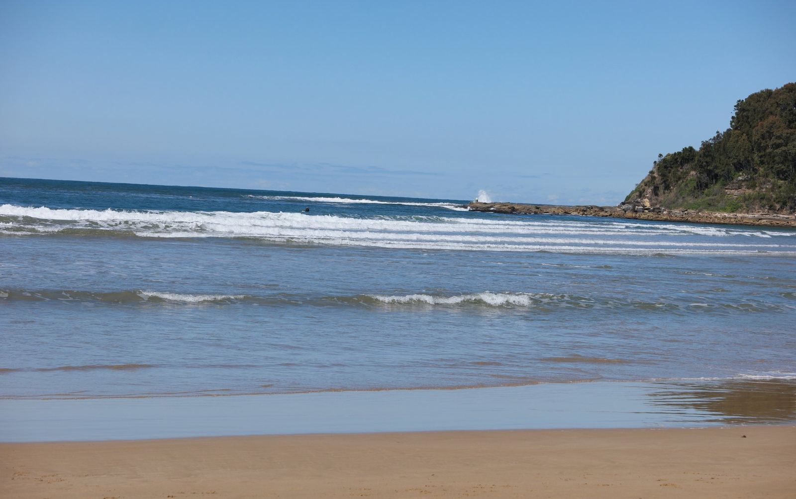 Small clean surf breaking along an empty stretch of sand under a pale sky