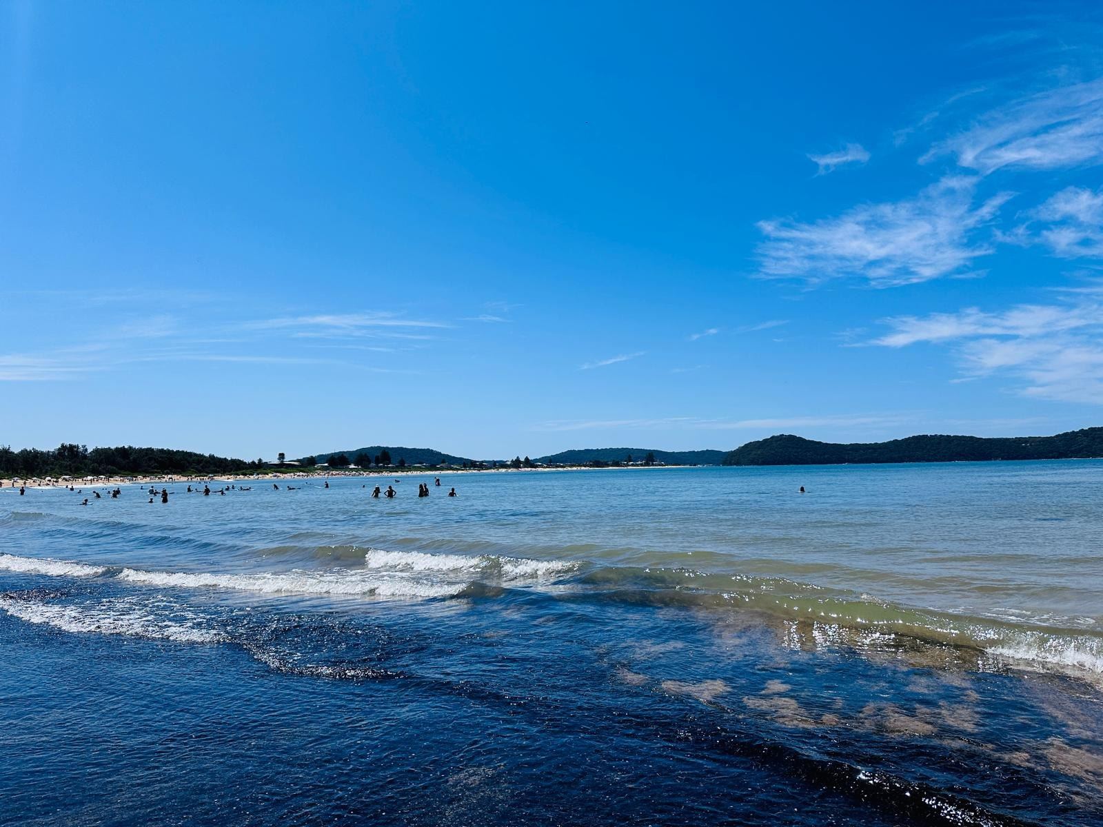 Lines of small swell running in towards the beach with swimmers out beyond the break
