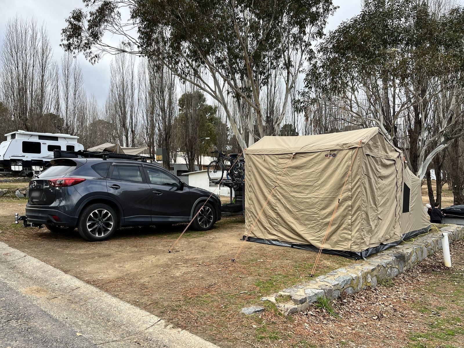 An Oztent RX-5 with its front room pitched on a bare winter site, the car and bike trailer parked alongside under leafless trees