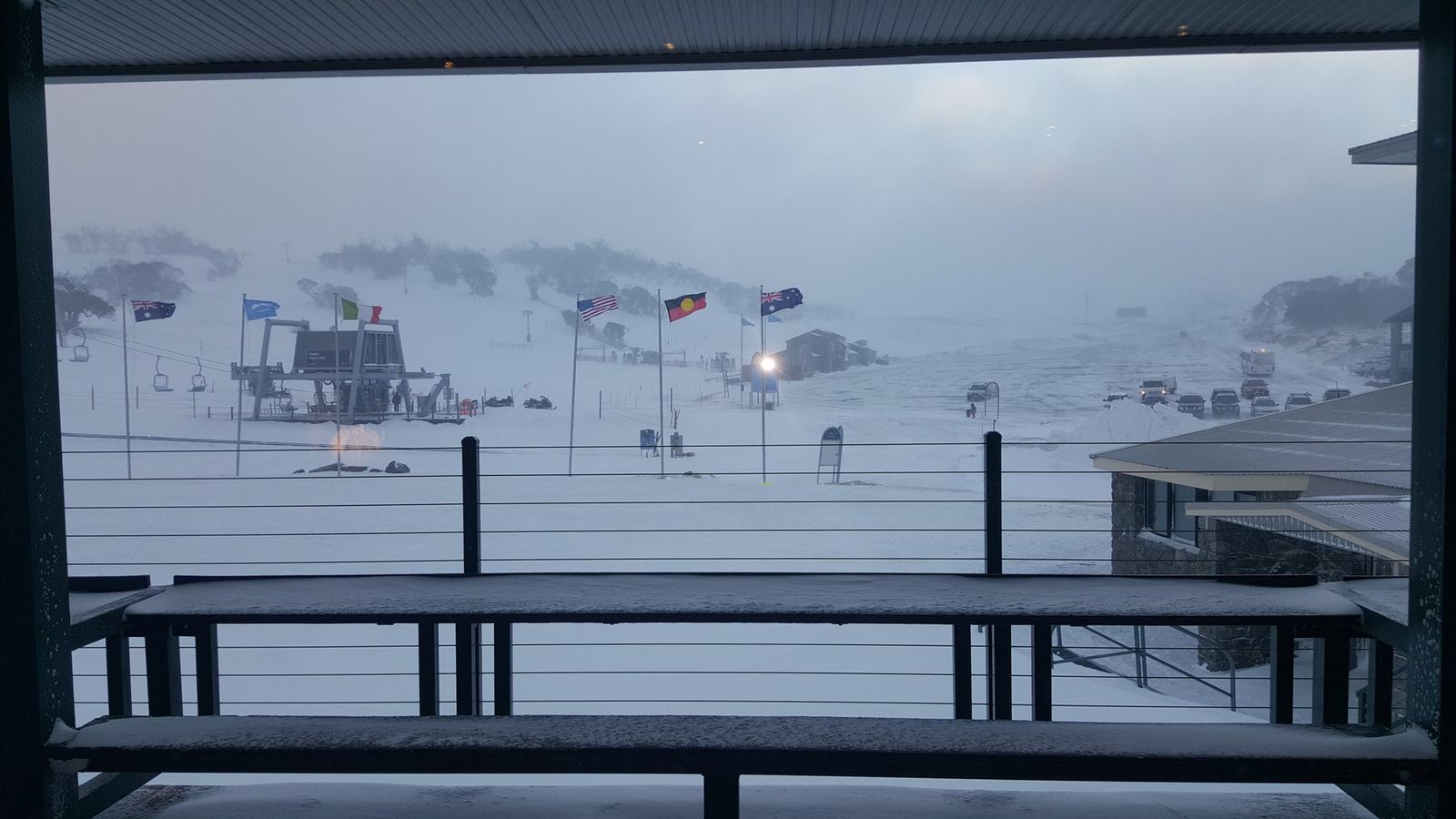 Snow falling across the Perisher runs and lift towers, seen from a lodge balcony at dawn