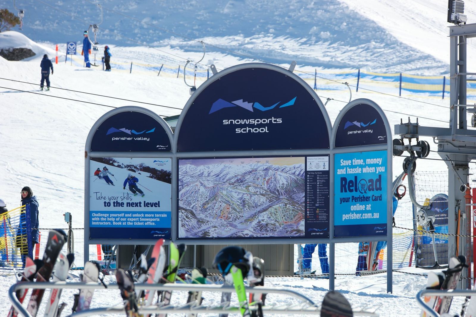 The Perisher snowsports school sign and trail map board standing beside the snow