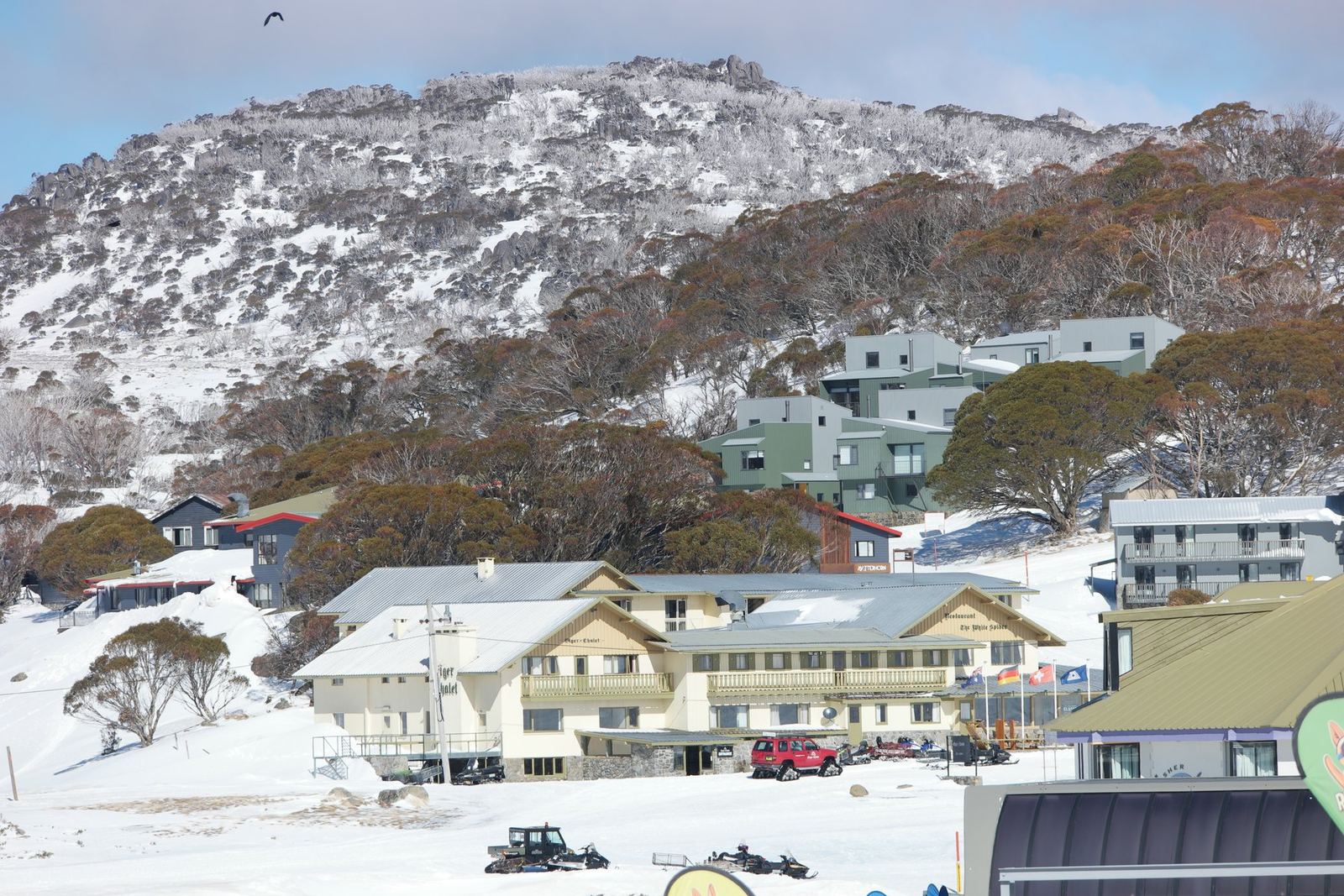 Perisher Valley lodges banked with snow below a bare treed ridge
