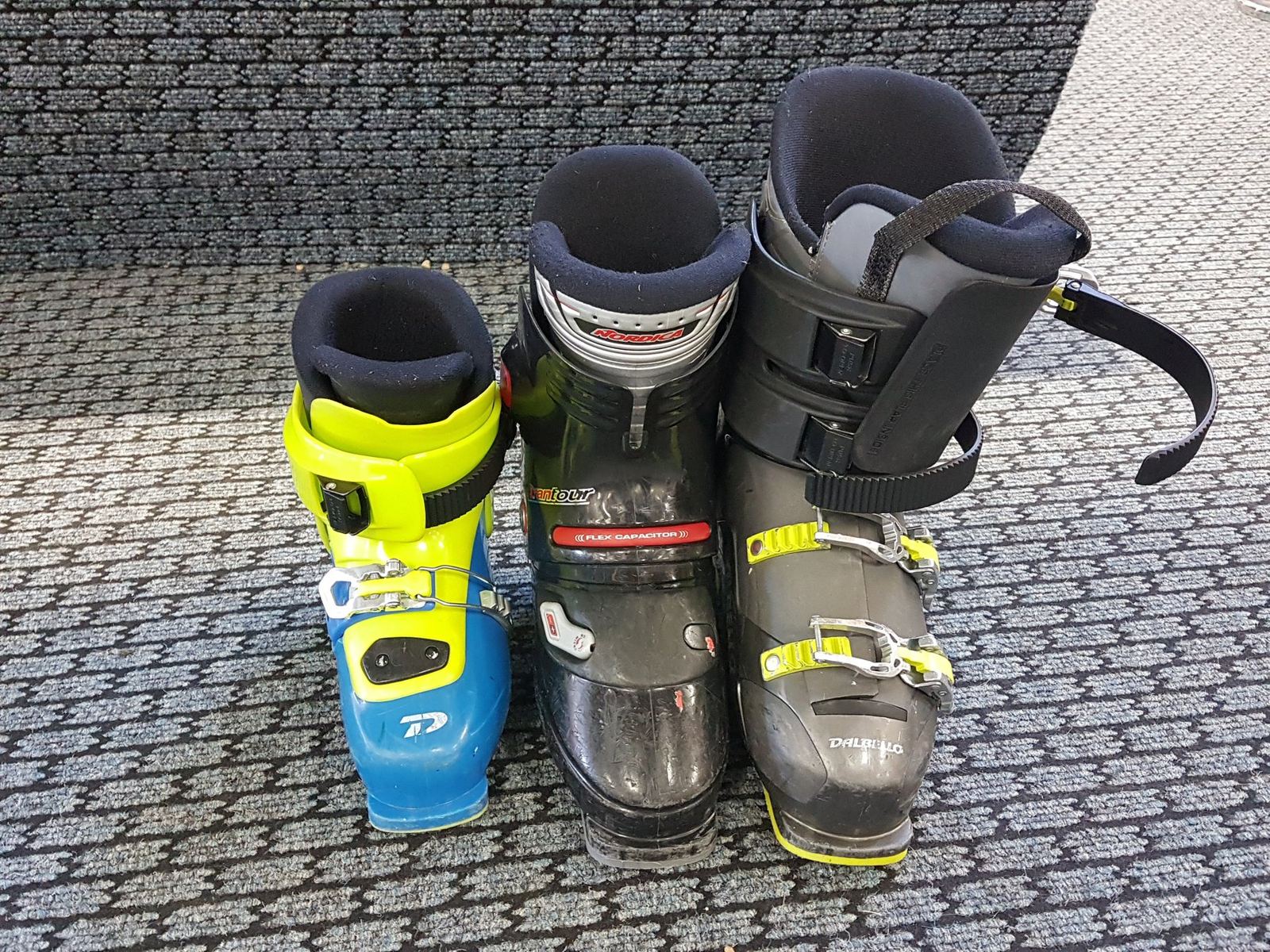 Three pairs of ski boots standing open on a patterned carpet to dry