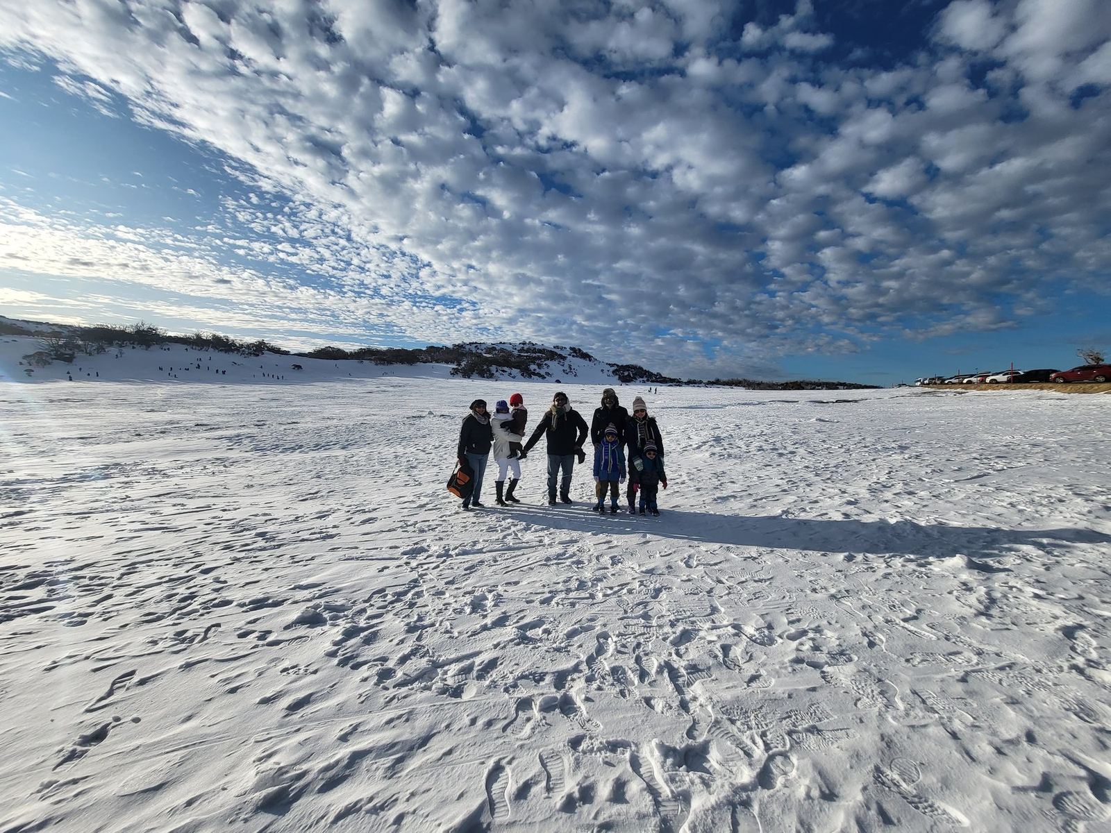 A wide snowfield with a few distant figures walking on it, under a mackerel sky of small even clouds