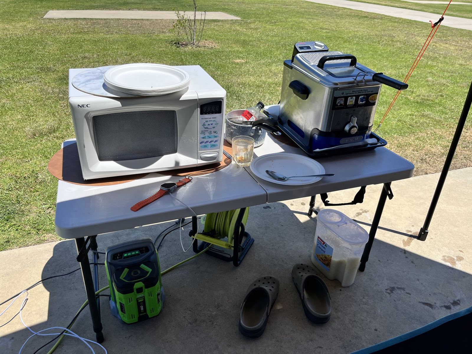 A microwave and an air fryer side by side on a camp table, both plugged into a portable power station on the ground