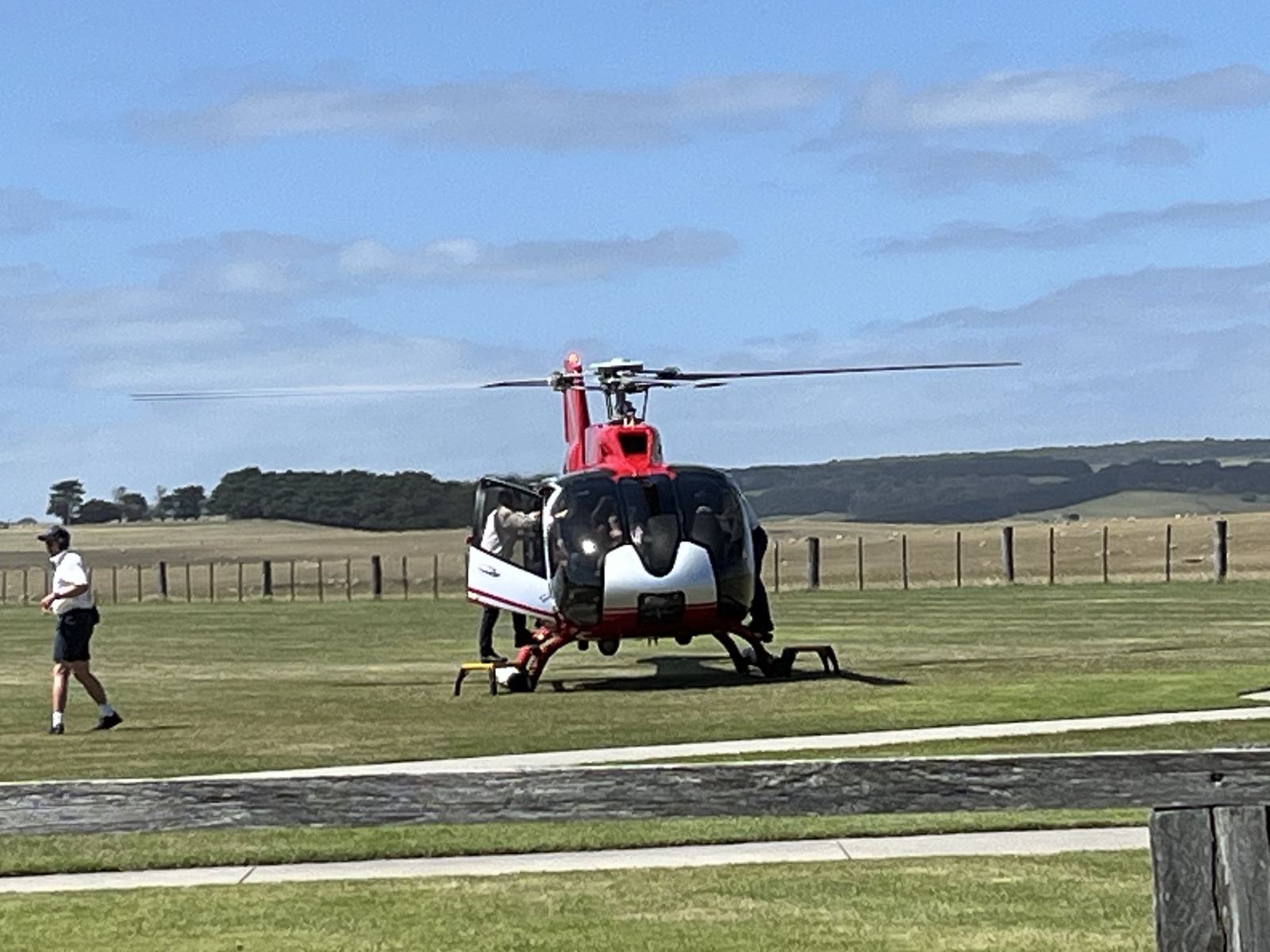 The same helicopter sitting on its pad with coastal paddocks and the sea behind